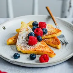 Goldbraune French Toast-Scheiben, bestäubt mit Puderzucker und garniert mit frischen Beeren. Ein perfektes Frühstück, das Lust auf mehr macht.