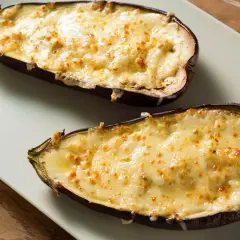 Dos mitades de berenjenas rellenas de carne, gratinadas con queso dorado y burbujeante, listas para disfrutar.