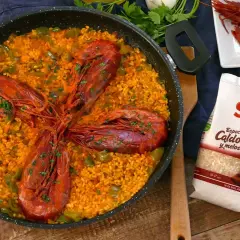 Arroz con carabineros en paellera, con pimientos verdes y perejil picado. A un lado, carabineros frescos y un paquete de arroz SOS.