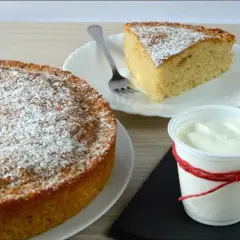 Torta 7 vasetti soffice e profumata, spolverata di zucchero a velo. Una fetta invitante e una coppetta di yogurt completano la scena.