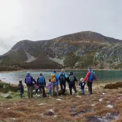 Un grupo de personas, incluyendo niños, disfruta de excursiones en familia junto a un lago rodeado de montañas.