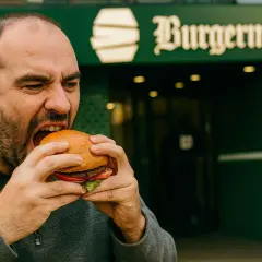 Mężczyzna z pasją wgryza się w soczystego burgera, zastanawiając się, skąd pochodzą hamburgery.