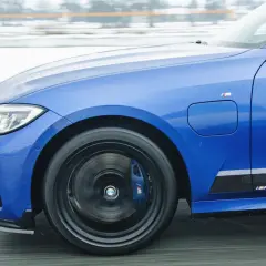 Niebieskie BMW 330e z napisem M Performance na progu, w ruchu drogowym.
