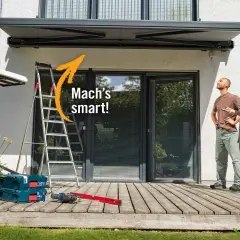Sonnenschutz Terrasse Ideen: Mann und Frau blicken nach oben, während Werkzeug und Leiter auf der Holzterrasse bereitstehen.