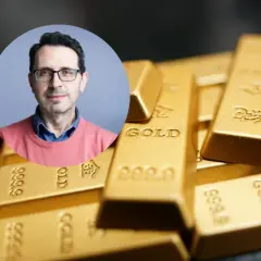 Mężczyzna w okularach na tle sztabek złota. Czy złoto traci na wartości? Analiza eksperta.