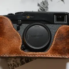 Skórzane etui na aparat Fujifilm X Pro1, z widocznym obiektywem X Mount, leży na stronach książki z historycznymi zdjęciami.