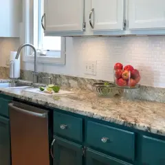 A kitchen with a white subway tile backsplash, granite countertops, and teal cabinets. A bowl of apples sits on the counter.