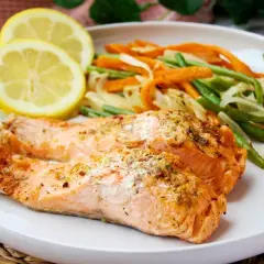 Dos filetes de salmón al microondas con hierbas, acompañados de zanahorias y judías verdes, y rodajas de limón.