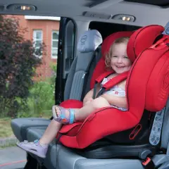Ein lächelndes Kind sitzt sicher in einem roten Kindersitz im Auto. Perfekt für den nächsten Ausflug oder als Taxi Kindersitz.