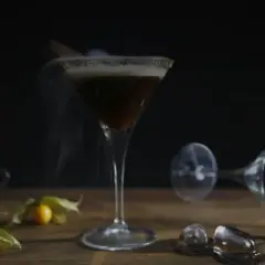 Ein dampfender Espresso Martini mit Zimt und einer kleinen Espressotasse daneben.