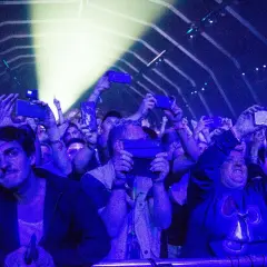 Tłum na fest festiwalu nagrywa koncert telefonami. Światła sceny oświetlają twarze ludzi.