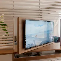 Ein moderner Wohnraum mit einem drehbaren Fernseher, der sich elegant in die Holzverkleidung integriert. Callas und dezente Beleuchtung schaffen eine ruhige Atmosphäre, ideal, um den Fernseher verstecken zu können.