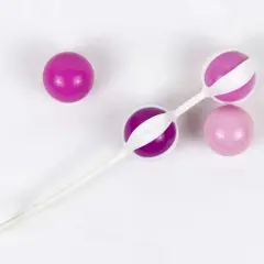 Trois boules de geisha, deux roses et une violette, sur fond blanc.