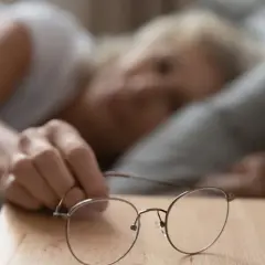 Kobieta sięga po okulary, czując wysokie tętno po przebudzeniu.