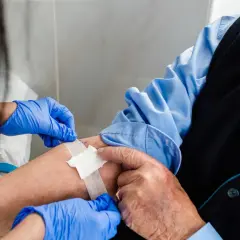 Pielęgniarka zakłada plaster na ramię starszego mężczyzny po pobraniu krwi. Wyniki badań, w tym trójglicerydy norma, są kluczowe dla zdrowia.