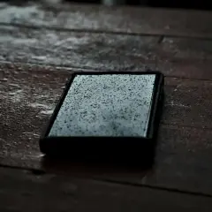 Telefon leży na mokrym drewnianym stole, pokryty kropelkami deszczu. Jego obudowa z certyfikatem IPX5 zapewnia mu ochronę przed wilgocią.