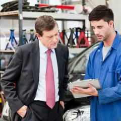 Un homme en costume discute avec un mécanicien dans un garage. Il semble qu'il soit sur le point de porter plainte contre un garage automobile.