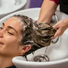 Una mujer sonríe mientras le lavan el pelo en un salón. La frecuencia con la que hay que lavarse el pelo varía, pero este momento de spa parece perfecto.