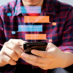 Mężczyzna trzyma smartfon, a nad nim pojawiają się dymki czatu. Dowiedz się, jak zaktualizować Messengera na telefonie, aby zawsze być na bieżąco.