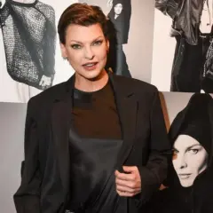 Linda Evangelista hoy, posando con confianza frente a un collage de sus icónicas fotos de moda.