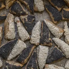 En bakplåt full med bröd som jäsa deg, täckta med sesamfrön och vallmofrön.