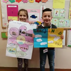 Dzieci prezentują swoje prace: dziewczynka z kwiatem "Wszystko o mnie", chłopiec z kolorowymi kartkami "Gracjan". To ich autoprezentacja o sobie do szkoły.