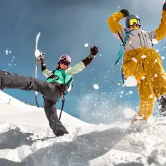 Dwóch narciarzy w akcji na śniegu, jeden z nartami, drugi na snowboardzie, z rozbryzgami śniegu.