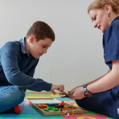 Chłopiec i terapeutka bawią się klockami w sali terapeutycznej.