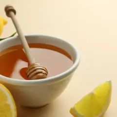 Un remède naturel contre le mal de gorge : un bol de miel doré avec une cuillère en bois, entouré de citrons frais et de feuilles vertes.