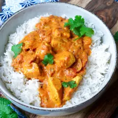 Schüssel mit duftendem Reis und cremigem Chicken Tikka Masala, garniert mit frischem Koriander. Daneben Mandelsplitter, Knoblauch und Ingwer.