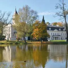 Pałac w jesiennej scenerii nad jeziorem, część Bolimowskiego Parku Krajobrazowego. Kaczka pływa po wodzie.