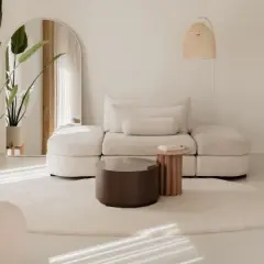 Ein helles Wohnzimmer im Japandi-Stil mit einem beigen Sofa, einem runden Teppich und einer großen Topfpflanze.