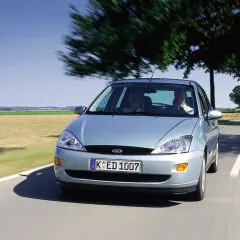 Srebrny Ford Focus MK1 1.6 benzyna w ruchu po wiejskiej drodze, z dwoma osobami w środku.