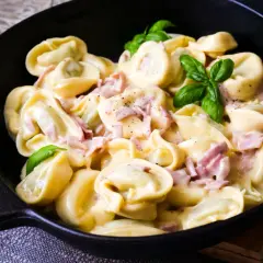 Frische Tortellini mit Schinken in cremiger Sauce, garniert mit Basilikum. Ein Genuss, wenn man Tortellini selber machen möchte.