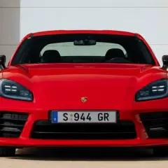 El llamativo Porsche 944 rojo, con su distintivo frontal y faros LED, se exhibe frente a una puerta de garaje blanca y paredes naranjas.