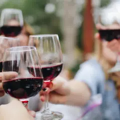 Des mains lèvent des verres de vin rouge pour un apéro convivial.