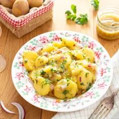 Salade de pommes de terre avec oignons rouges et persil, servie dans une assiette fleurie.