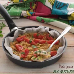 Alici gratinate in padella con pomodorini e pangrattato, un piatto semplice e gustoso.