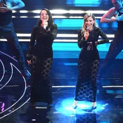 Due sorelle cantanti italiane, vestite con abiti neri scintillanti, si esibiscono sul palco con ballerini sullo sfondo.