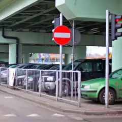 Czerwony samochód zbliża się do parkingu, gdzie stoi znak b2. Zielony samochód zaparkowany jest pod wiaduktem.