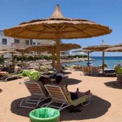 Egipt last minute all inclusive najtaniej: piaszczysta plaża z leżakami i parasolami, turkusowe morze, hotel w tle. Idealne miejsce na relaks.