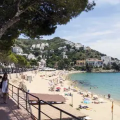 Gente disfrutando del sol y el mar en la playa de la punta, con casas blancas en la colina.