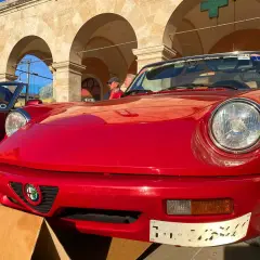 Dreaming of renting a car in Italy? This classic red Alfa Romeo convertible, parked under arched buildings, evokes the perfect Italian road trip.