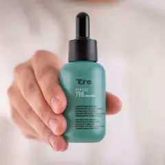 Mano sostiene frasco verde con peptidos para el pelo, concentrado anticaída T98 de Tahe.
