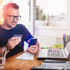 Mężczyzna z kartą płatniczą i telefonem w ręku, jakby planował zakupy. Nie ma tu żadnych provident złodziei, tylko domowe biuro.