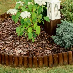 Natürliche beeteinfassung ideen: Holzrundlinge grenzen ein Blumenbeet mit Hortensien und Ziergräsern ab.