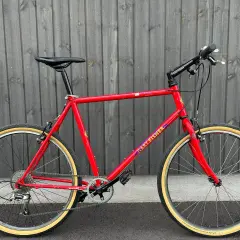 A vintage red Gary Fisher Advance mountain bike with tan tires stands against a wooden fence.