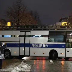 Ein Bus mit der Aufschrift "ADENAUER SRP+" steht im Dunkeln. Eine Person fotografiert ihn.