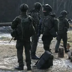 Żołnierze w kamuflażu stoją przy torach kolejowych. Ich zarobki w wojsku pozwalają na wyposażenie i szkolenia.