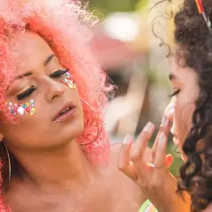 Kolorowy makijaż na festiwal z brokatem i kamyczkami na twarzy. Różowe włosy i błyszczące oczy.